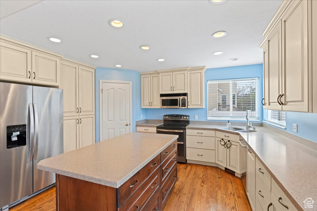 Kitchen with stainless steel appliances, cream cabinets, a sink, light wood finished floors, and recessed lighting
