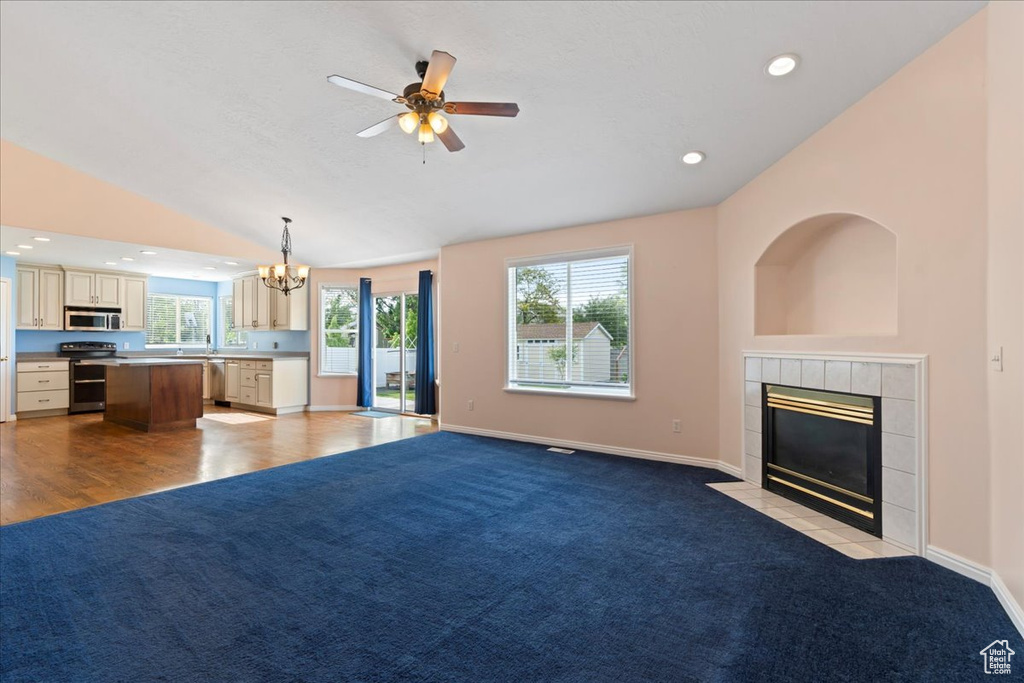 Unfurnished living room featuring a tiled fireplace, a chandelier, a ceiling fan, vaulted ceiling, and baseboards