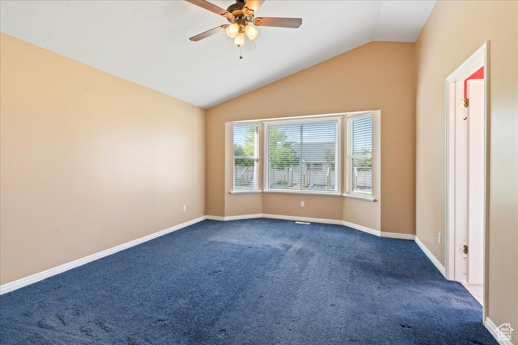 Spare room with dark carpet, vaulted ceiling, ceiling fan, and baseboards