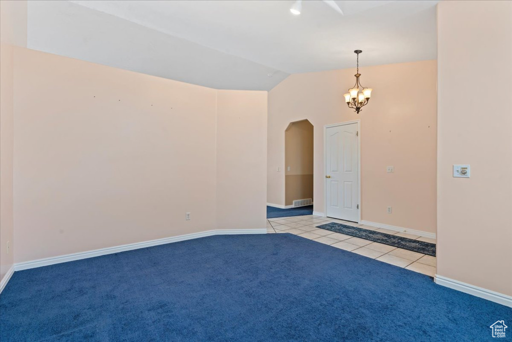 Empty room with arched walkways, lofted ceiling, a chandelier, light tile patterned floors, and baseboards