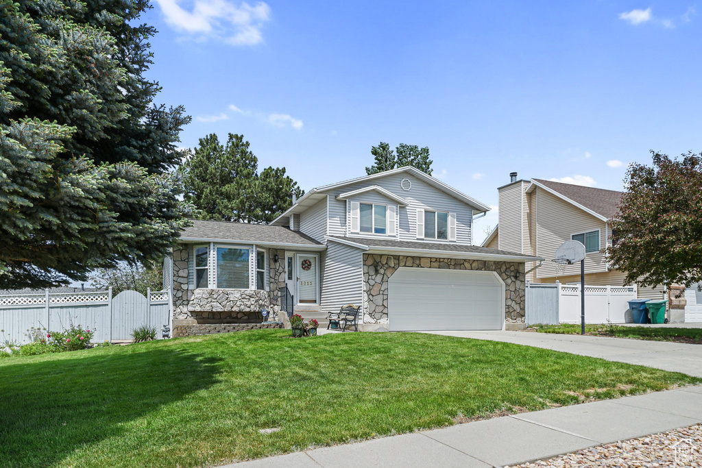 Split level home with stone siding, a garage, concrete driveway, and a gate