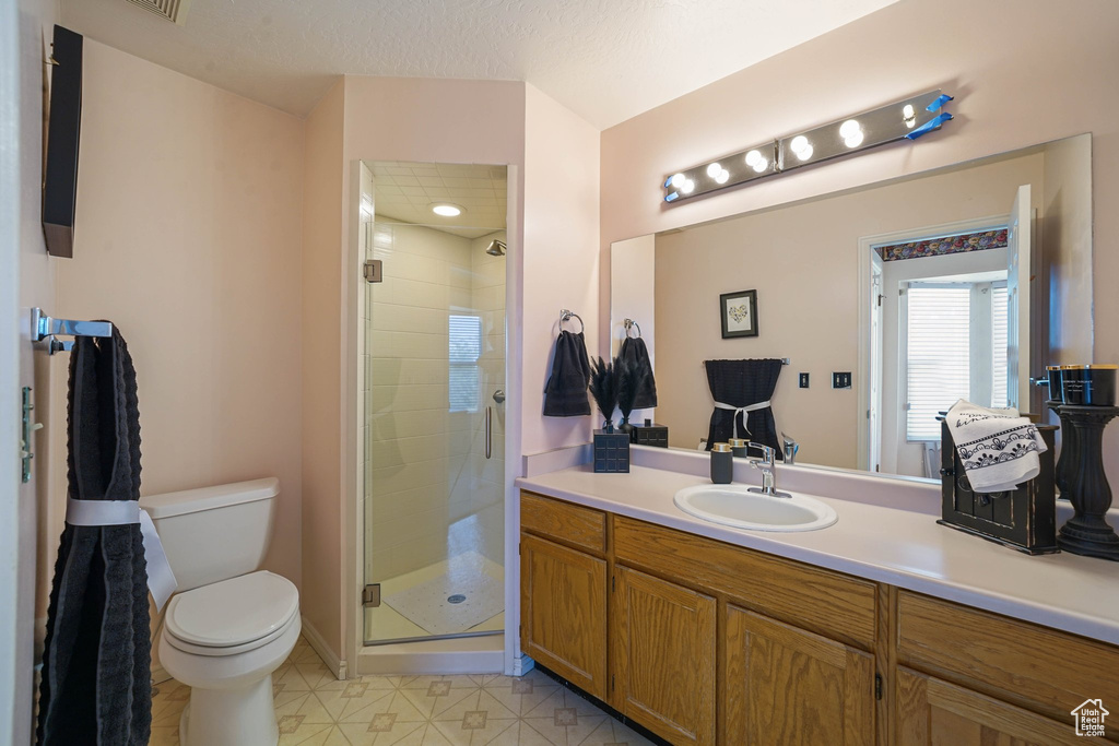 Bathroom featuring toilet, vanity, a stall shower, and tile patterned floors