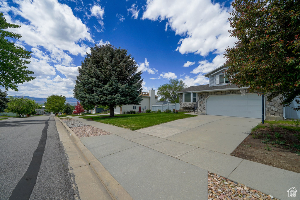 View of front of home with stone siding, driveway, a front lawn, and an attached garage