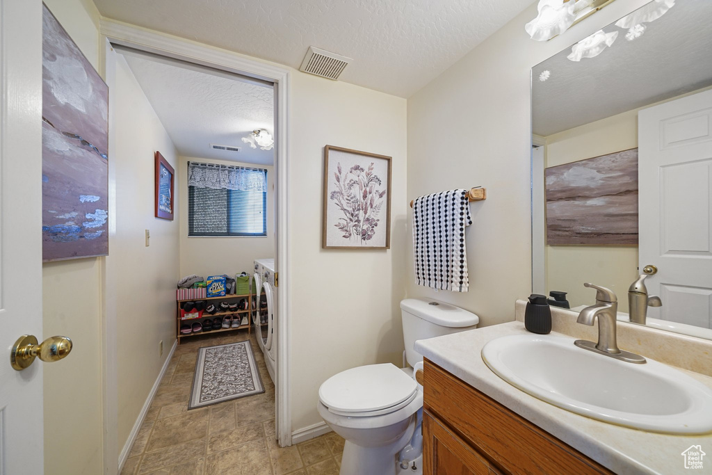 Bathroom with separate washer and dryer, vanity, toilet, baseboards, and a textured ceiling