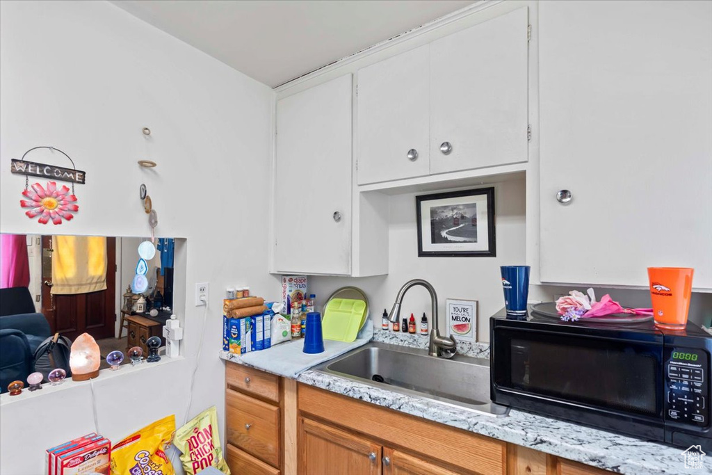 Kitchen with a sink, black microwave, and white cabinetry