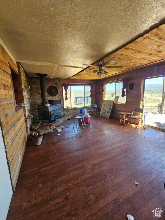 Living room with a wood stove, a ceiling fan, wooden walls, hardwood / wood-style flooring, and a textured ceiling