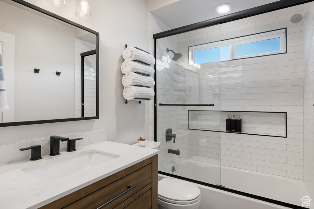 Bathroom with vanity, toilet, and combined bath / shower with glass door