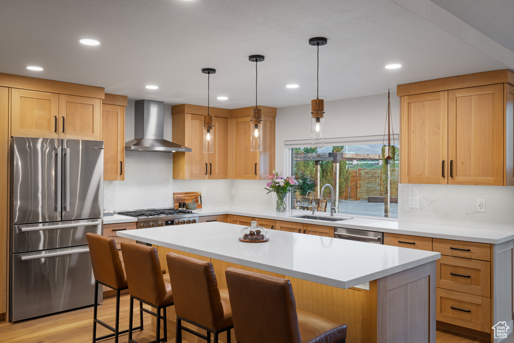 Kitchen featuring appliances with stainless steel finishes, wall chimney exhaust hood, a sink, a kitchen breakfast bar, and a kitchen island