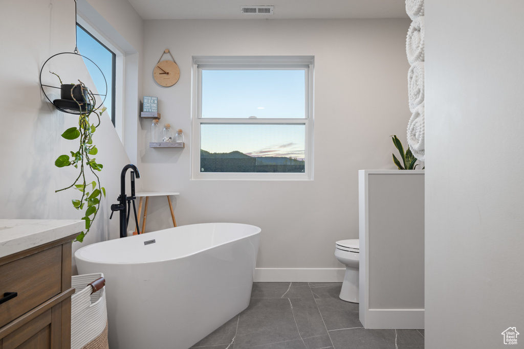 Full bath with a soaking tub, baseboards, vanity, toilet, and tile patterned flooring