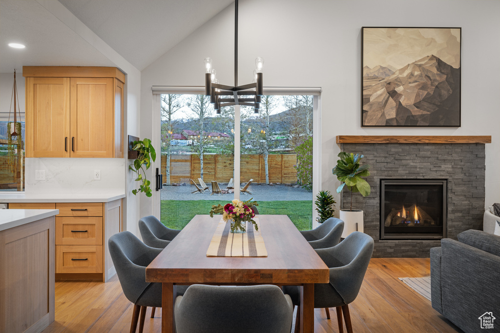 Dining space with high vaulted ceiling, light wood finished floors, a stone fireplace, and recessed lighting