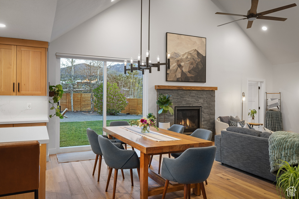 Dining room featuring high vaulted ceiling, recessed lighting, ceiling fan, a stone fireplace, and light wood-type flooring