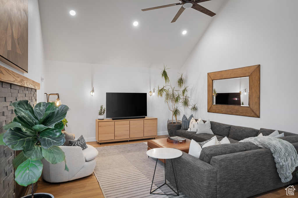 Living room featuring a ceiling fan, high vaulted ceiling, wood finished floors, a fireplace, and recessed lighting