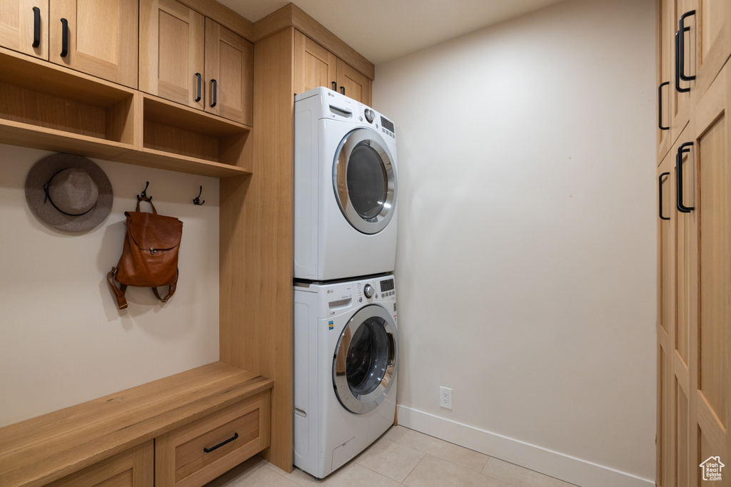 Washroom with stacked washer / drying machine, light tile patterned floors, baseboards, and cabinet space