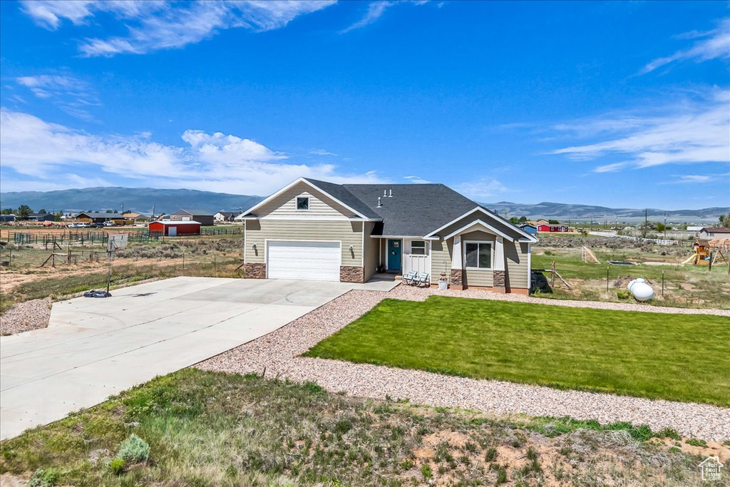 View of front of house with a mountain view, concrete driveway, a front yard, and a garage