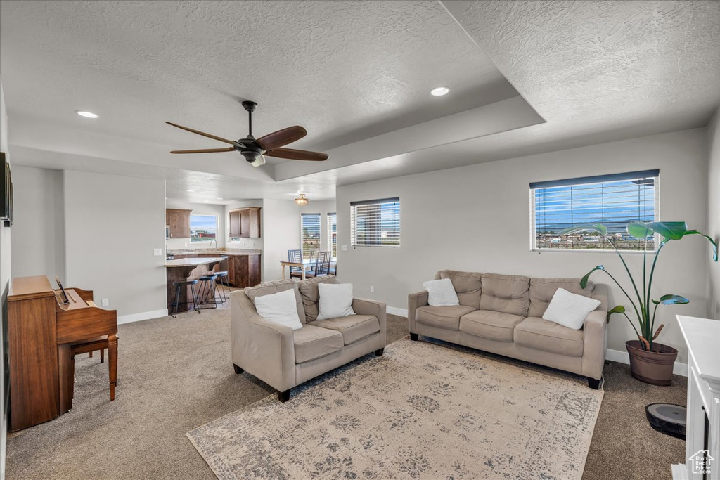 Living room with a textured ceiling, baseboards, a ceiling fan, light colored carpet, and recessed lighting