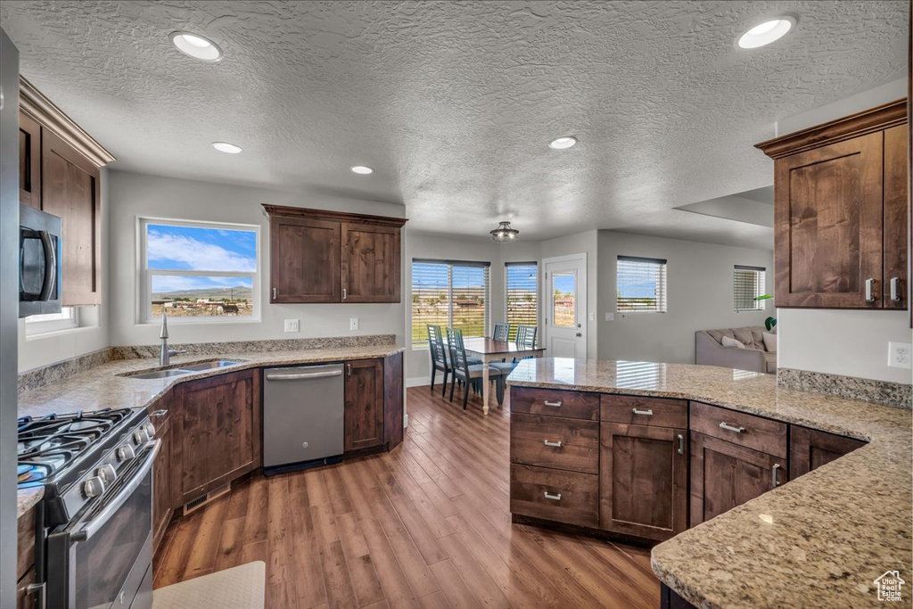 Kitchen with stainless steel appliances, a sink, light wood-style flooring, a textured ceiling, and light stone countertops