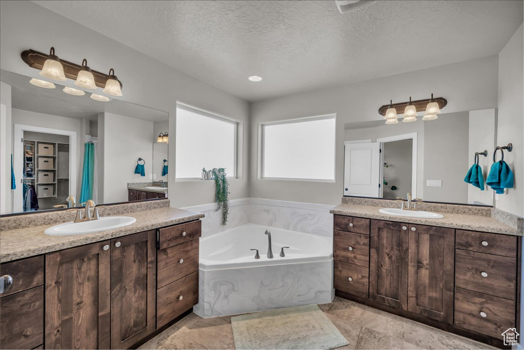 Full bathroom with two vanities, a garden tub, and a textured ceiling