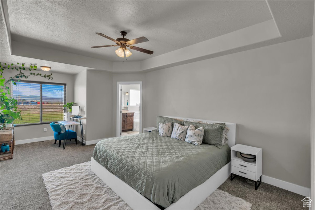 Carpeted bedroom featuring a tray ceiling, a textured ceiling, baseboards, and connected bathroom