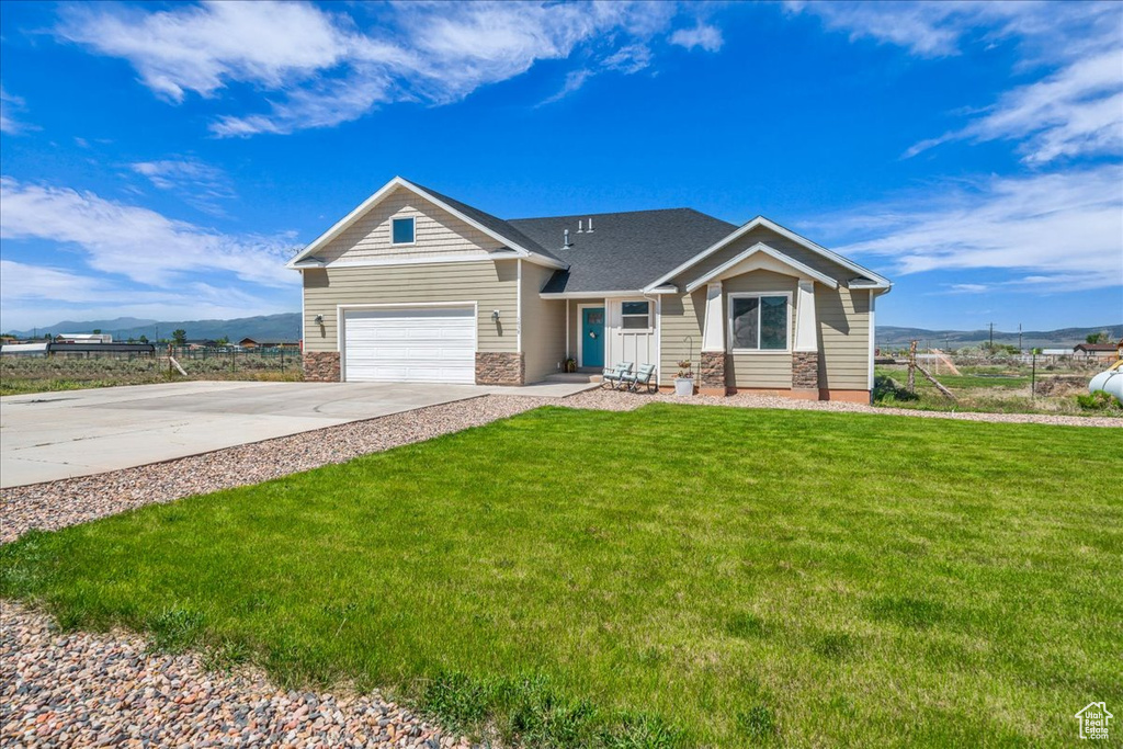 View of front facade featuring stone siding, a garage, concrete driveway, a front yard, and a mountain view