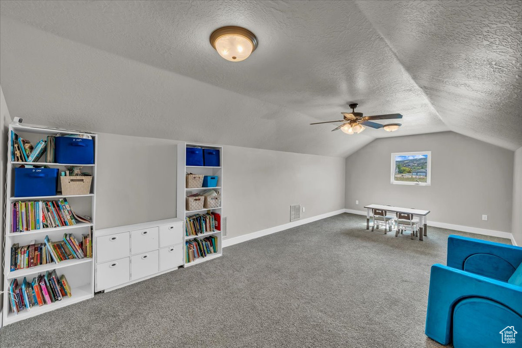 Playroom featuring a textured ceiling, vaulted ceiling, baseboards, carpet, and a ceiling fan