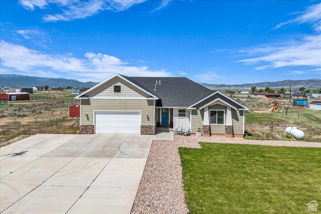 View of front of house with a mountain view, concrete driveway, and a front lawn