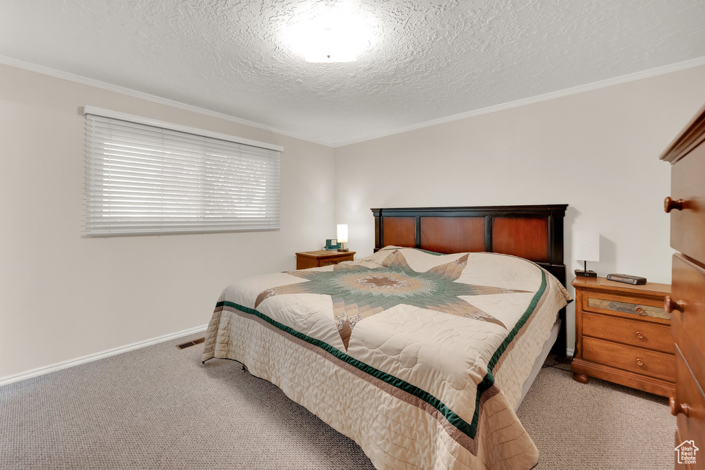 Bedroom featuring light carpet, crown molding, a textured ceiling, and baseboards
