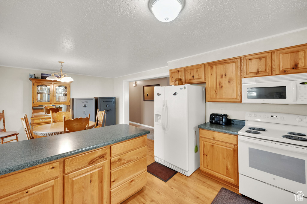 Kitchen with white appliances, dark countertops, light wood-style floors, a textured ceiling, and a chandelier