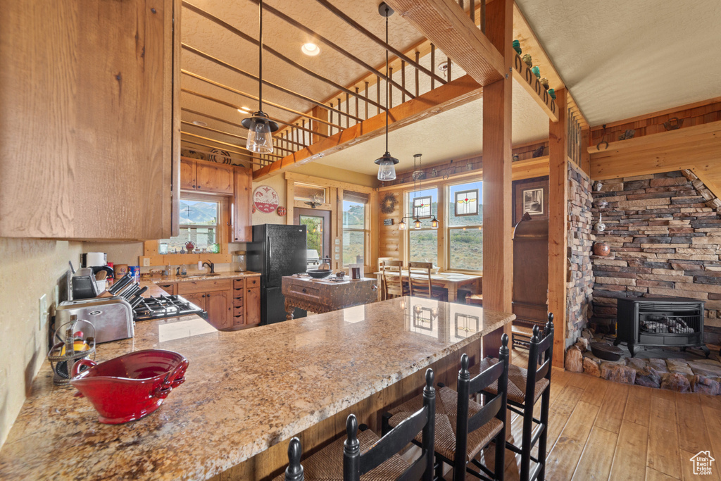Kitchen with freestanding refrigerator, light wood-style flooring, a peninsula, light stone counters, and a wood stove