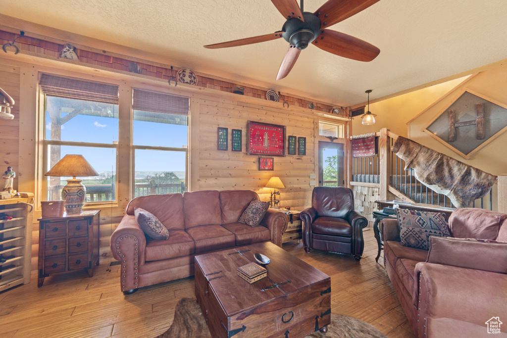 Living room with hardwood / wood-style floors, ceiling fan, wooden walls, and a textured ceiling