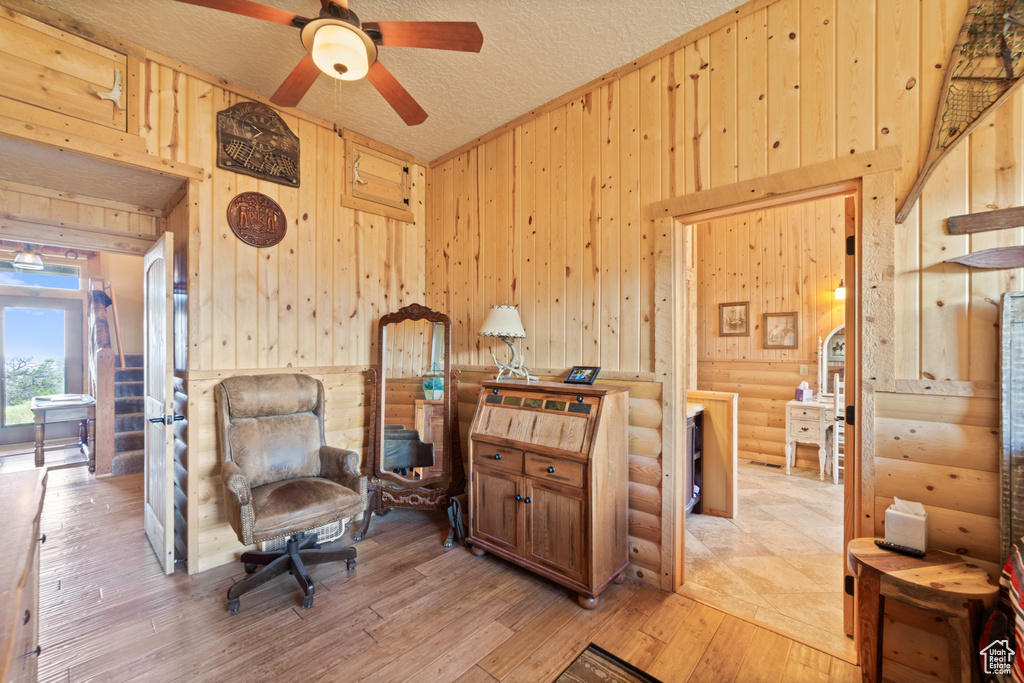 Living area with wooden walls, a ceiling fan, light wood-style flooring, log walls, and a textured ceiling
