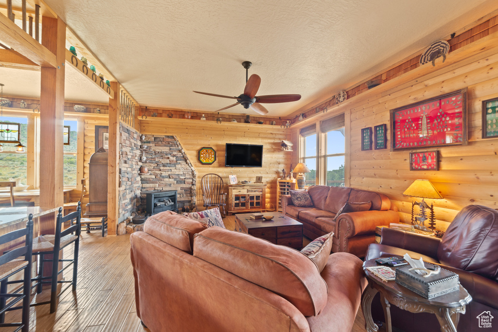 Living room with a wood stove, a ceiling fan, wood-type flooring, a textured ceiling, and wooden walls