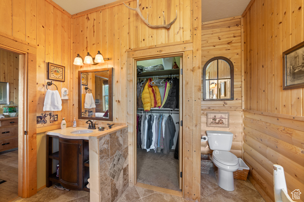 Full bath featuring wooden walls, toilet, vanity, radiator heating unit, and a spacious closet