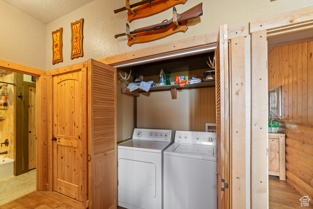 Clothes washing area with washing machine and clothes dryer, light wood-style floors, and a textured ceiling
