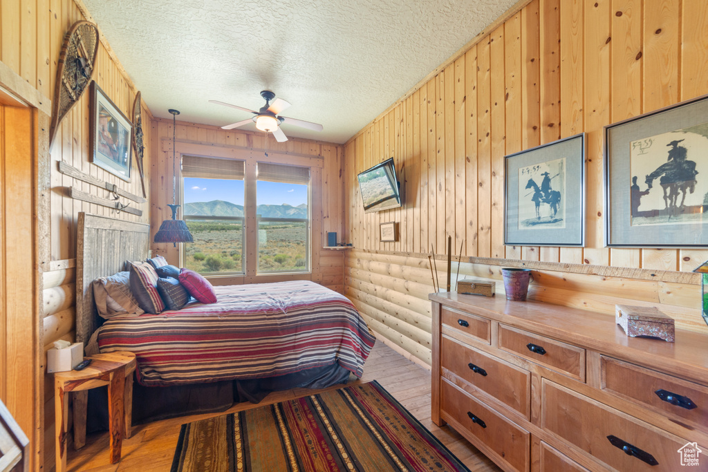 Bedroom with log walls, light wood-type flooring, and a textured ceiling