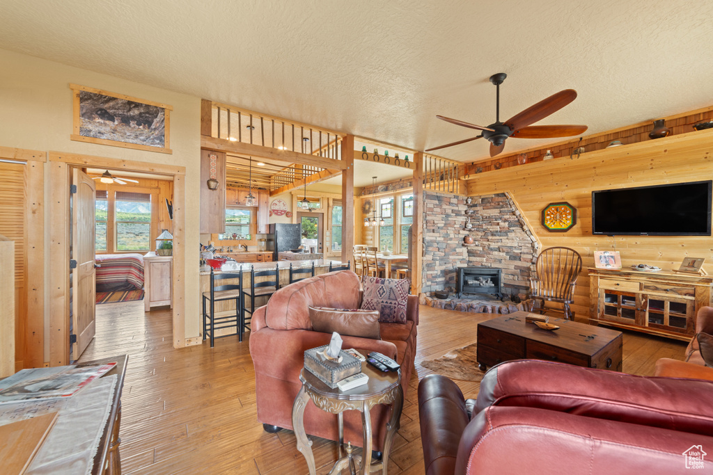 Living area featuring ceiling fan, a textured ceiling, a wood stove, wooden walls, and wood-type flooring