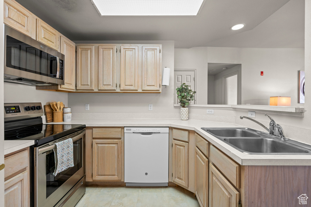 Kitchen with appliances with stainless steel finishes, light brown cabinets, a sink, light countertops, and recessed lighting
