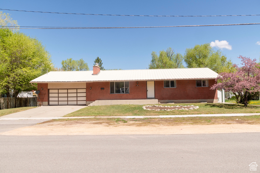 Ranch-style home featuring a garage, driveway, brick siding, a chimney, and a front lawn