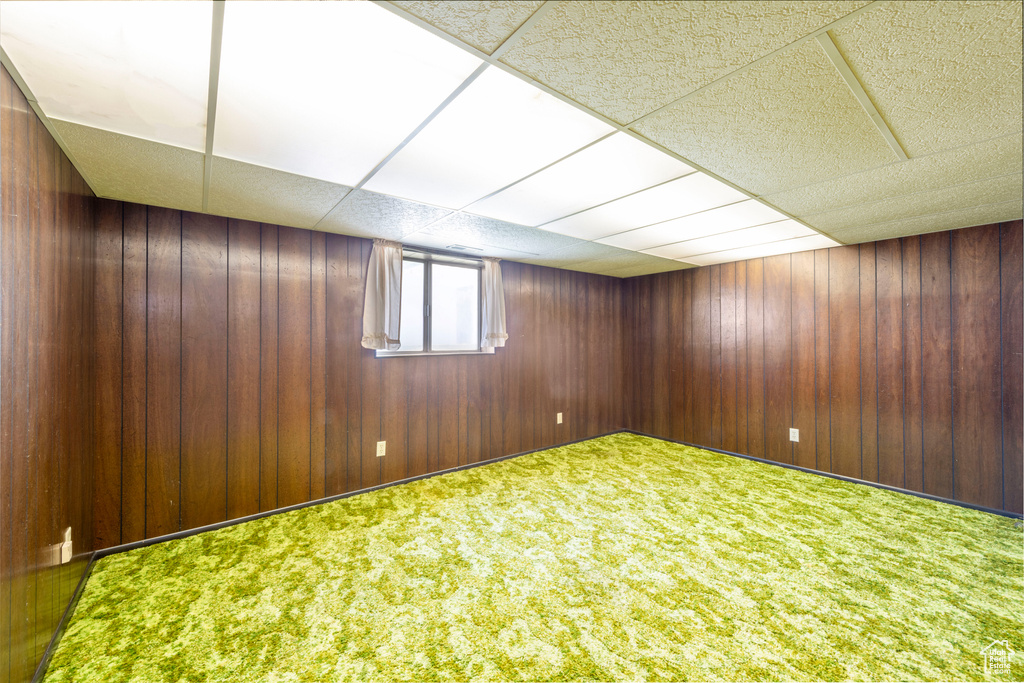 Below grade area featuring wooden walls, carpet flooring, and a drop ceiling