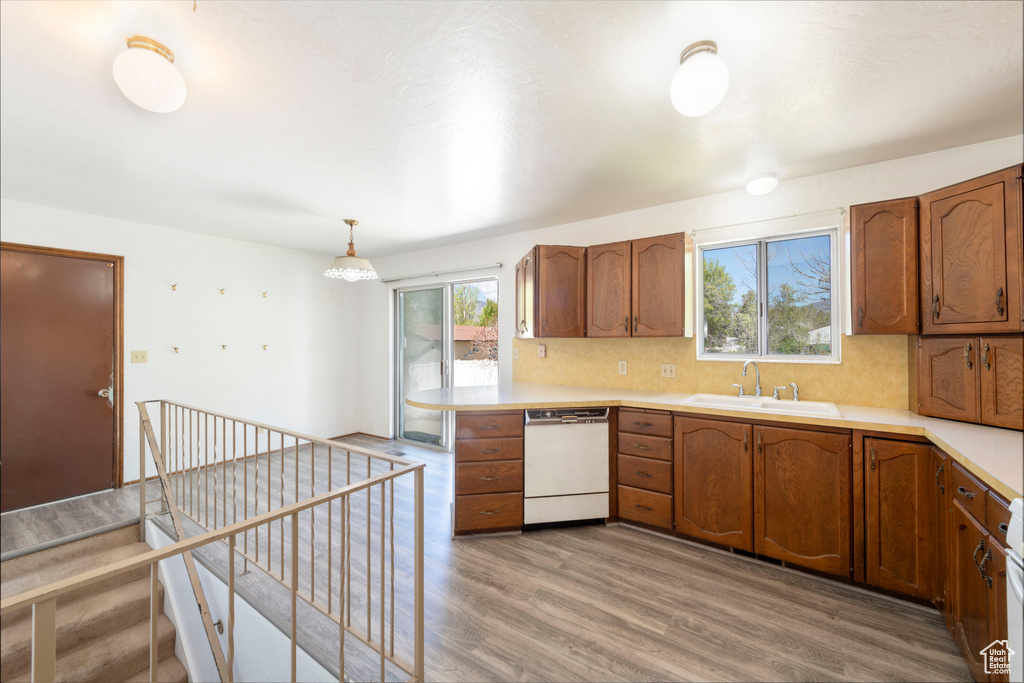 Kitchen with white dishwasher, a sink, light countertops, light wood finished floors, and brown cabinetry