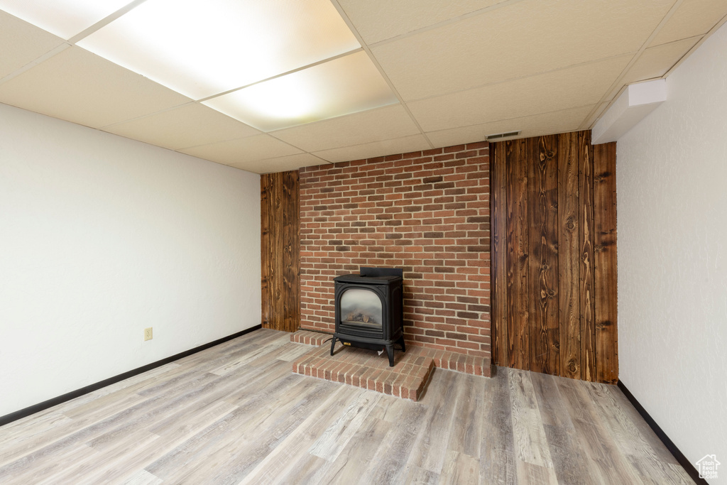 Unfurnished living room with a drop ceiling, a wood stove, wood finished floors, and baseboards