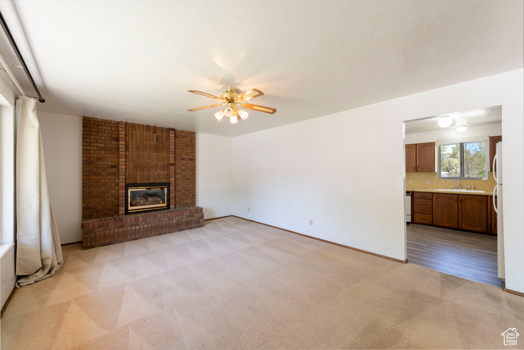 Unfurnished living room with light colored carpet, a ceiling fan, a brick fireplace, and baseboards