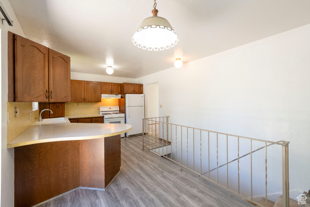 Kitchen featuring white appliances, a sink, under cabinet range hood, light wood-type flooring, and brown cabinets