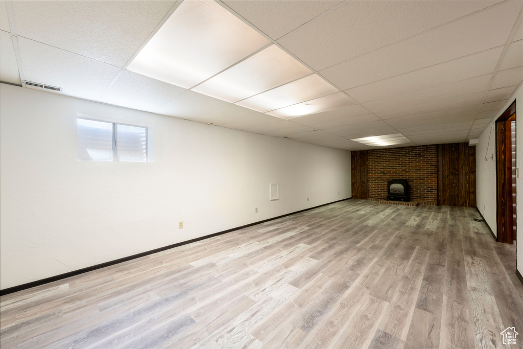 Basement featuring a paneled ceiling, light wood-style flooring, a brick fireplace, and baseboards