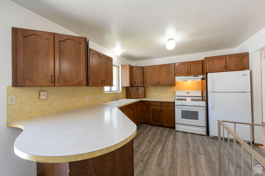 Kitchen featuring white appliances, under cabinet range hood, a sink, light countertops, and wood finished floors