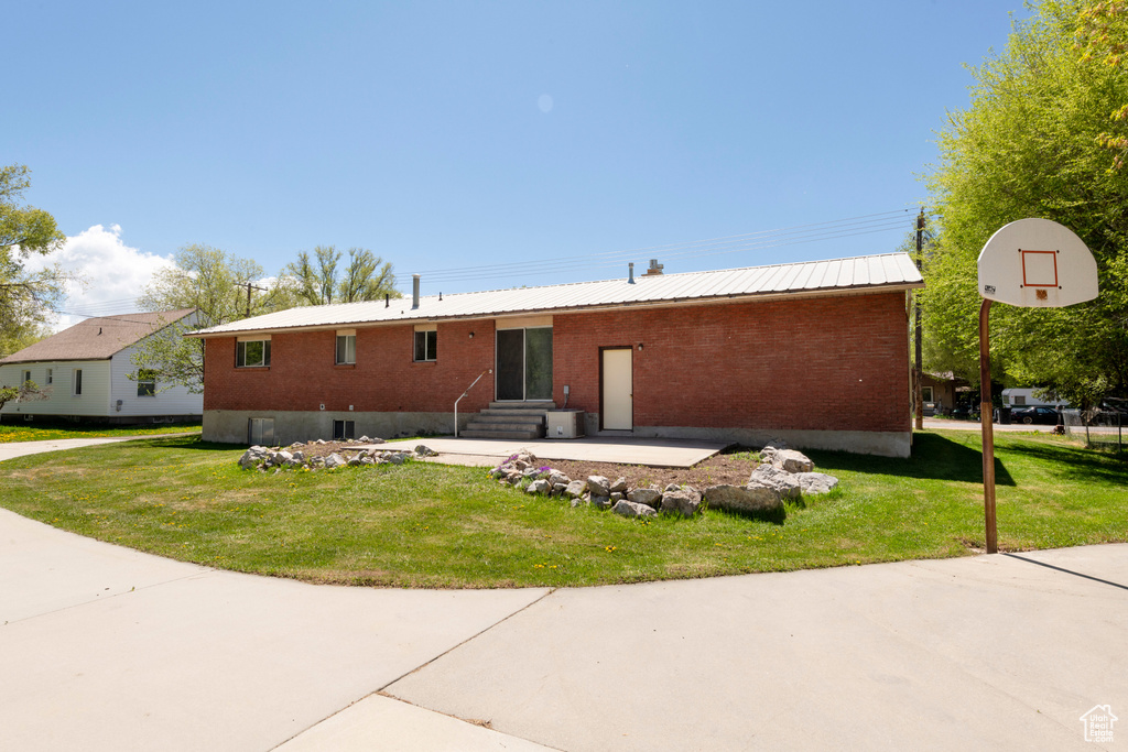 Rear view of property with entry steps, brick siding, a yard, and metal roof