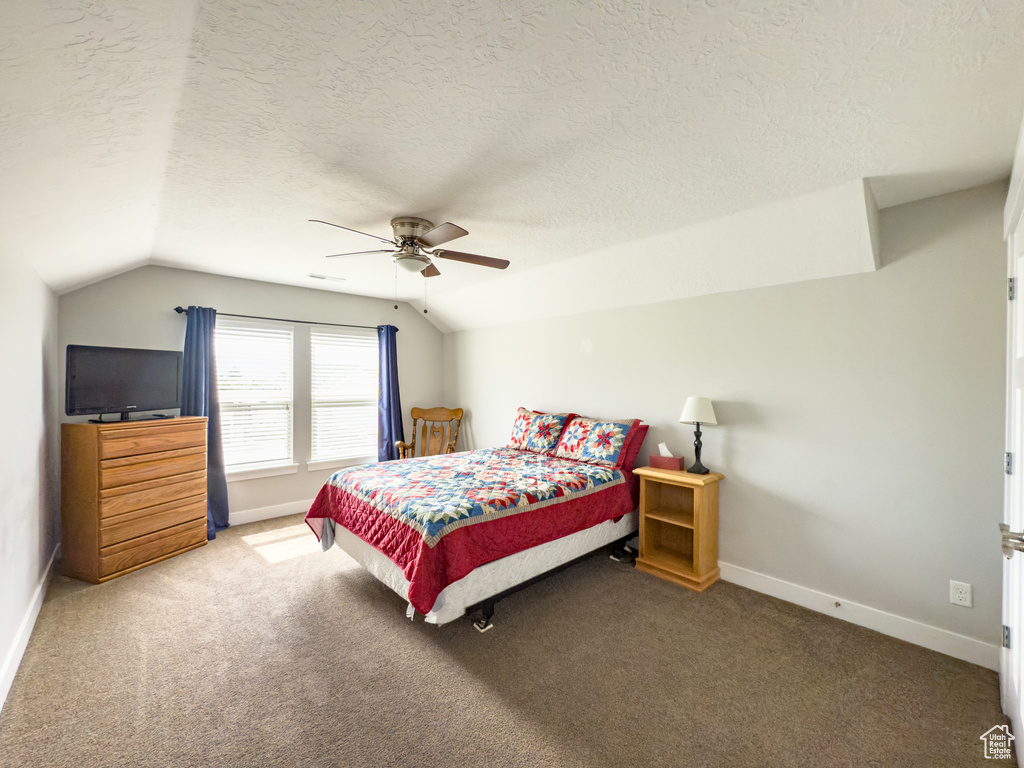 Bedroom featuring vaulted ceiling, a textured ceiling, carpet, baseboards, and ceiling fan