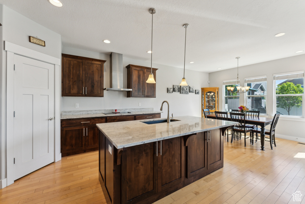 Kitchen featuring wall chimney range hood, a sink, light wood-style flooring, black electric cooktop, and recessed lighting