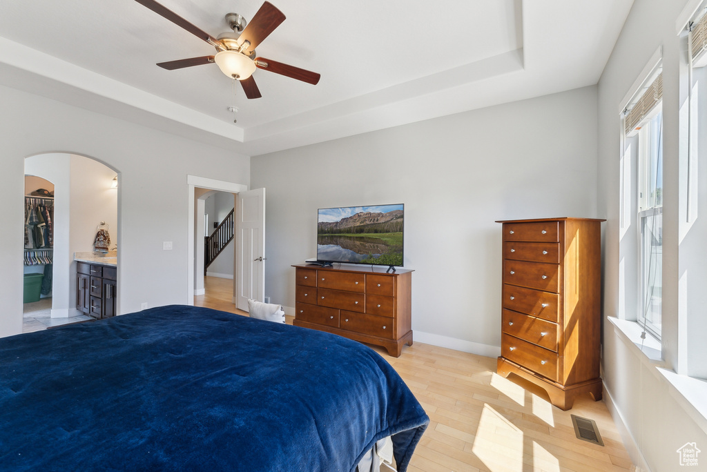 Bedroom featuring a tray ceiling, light wood-type flooring, arched walkways, ceiling fan, and baseboards