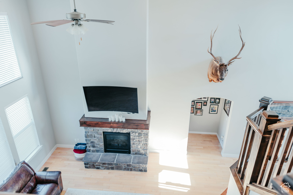 Living area featuring wood finished floors, a fireplace, ceiling fan, baseboards, and a high ceiling