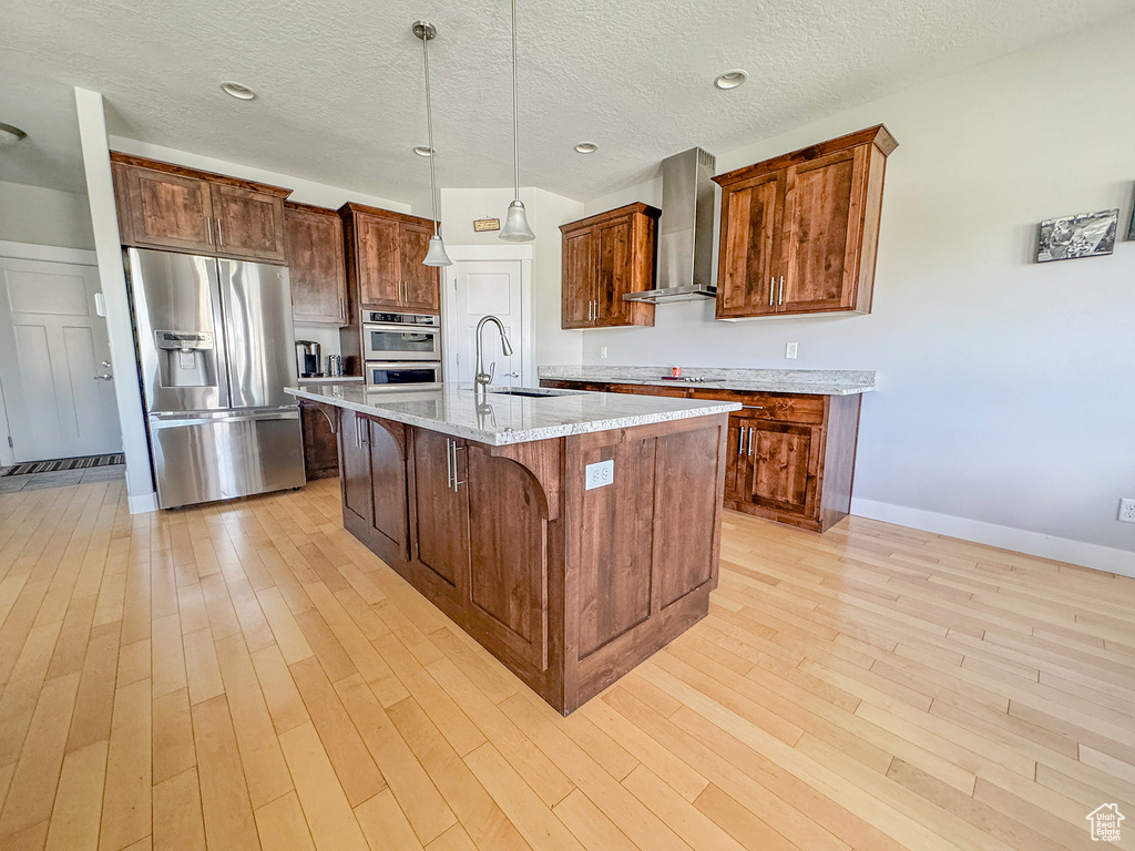 Kitchen with stainless steel appliances, wall chimney range hood, a sink, light wood-type flooring, and a kitchen breakfast bar
